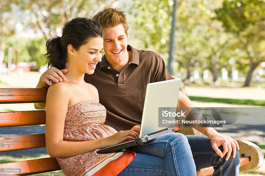 Smiling young couple using laptop at park  20-24 Years Stock Photo