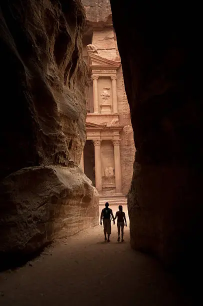 Silhouette  of two tourists walking along the Siq entering the lost city of Petra.