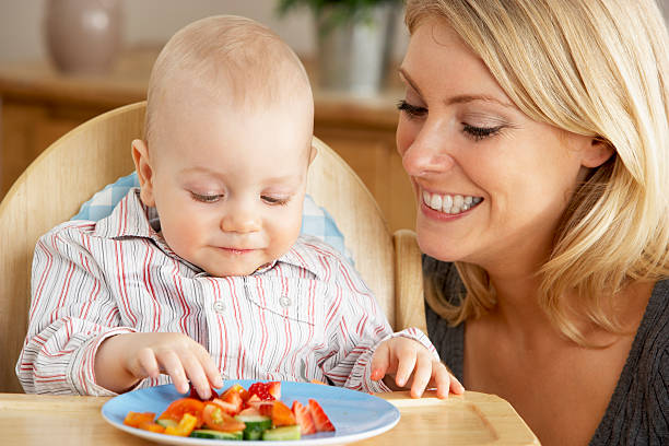Mother Feeding Son In High Chair stock photo