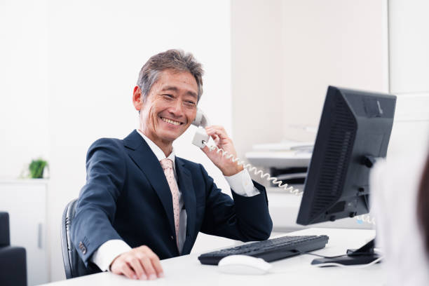 Man with a goofy smile listens on an old-fashioned phone. He might be hopelessly in love or chuckling at conspiracy theorists. Dreams of love or simply being elsewhere. Senior businessman in shirt and