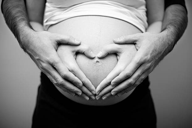 Man and woman's hands forming a heart over pregnant belly stock photo