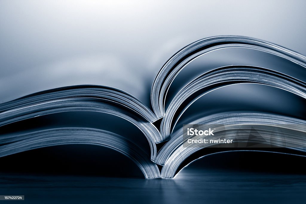Opened magazines A stack of magazines sitting on a wood table against a light background. Selective focus and extremely shallow depth of field. Tinted blue. Abstract Stock Photo