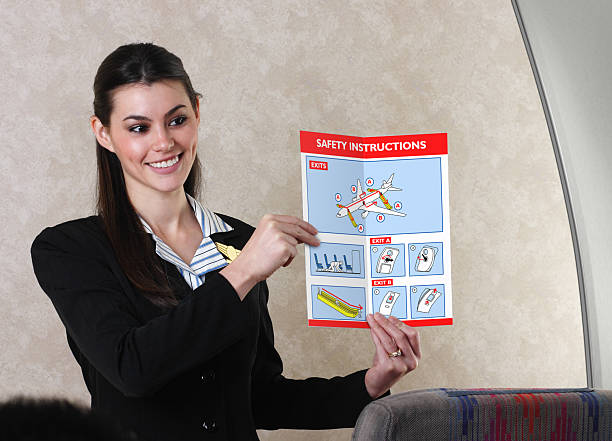 Flight Attendant And Safety Card An airline flight attendant reviewing a flight safety card before takeoff.  Note to inspector: Safety card is my original artwork. gchutka stock pictures, royalty-free photos & images