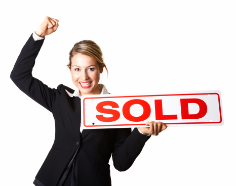 Portrait of a excited businesswoman holding sold sign board against white background