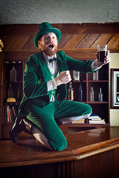 Irish / Leprechaun Character With Pint of Beer A "Leprechaun" looking man with red hair stands on top of the bar counter, in a funny full green suit with bow tie, perfect for St. Patrick's Day. tail coat photos stock pictures, royalty-free photos & images