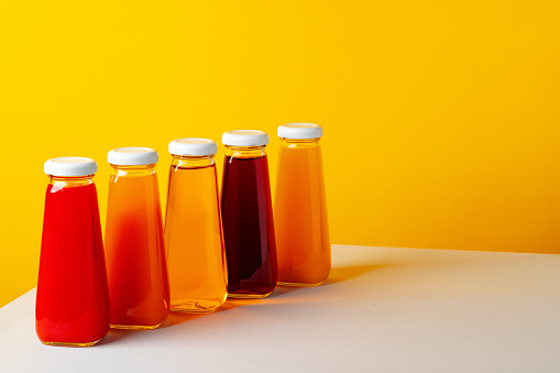Glass bottle with juice on white table against yellow background close up