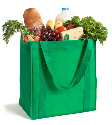 Cotton grocery tote bag with fresh vegetables, fruits, baguette and canned good on wooden background. Healthy food shopping, Eco-Friendly concept. Flat lay.