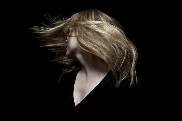 An abstract portrait of a little girl in black tossing blond hair. Studio shot on yellow background.