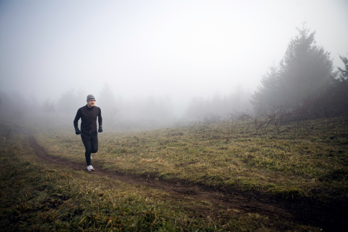 A young native Alaskan man runs up a small hill on a foggy morning.  Horizontal with copy space.