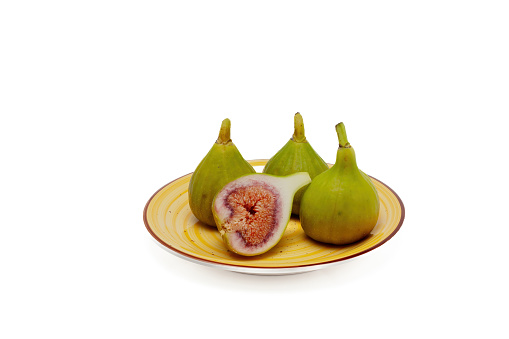Three green figs on a yellow plate and a ripe fig cut in half