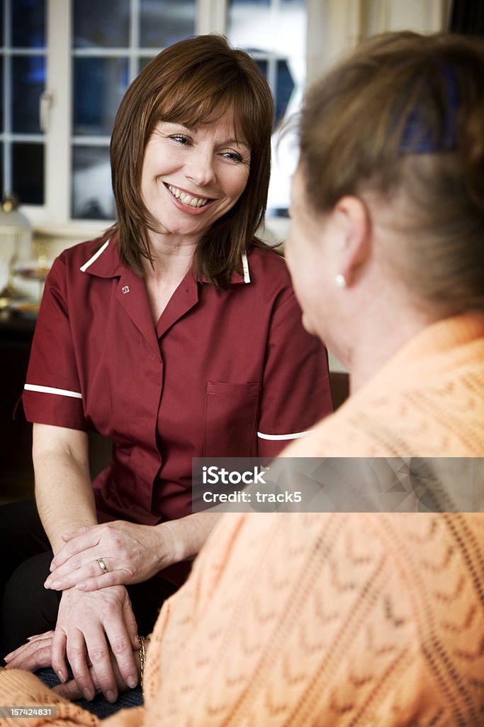 Servizio amichevole infermiera rassicurante di un senior con un sorriso - Foto stock royalty-free di 40-44 anni