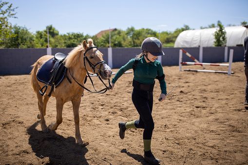 Girl running with her a brown horse outdoors on a ranch.