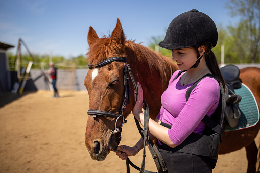 Teenage girl petting her brown horse outdoors on a ranch.