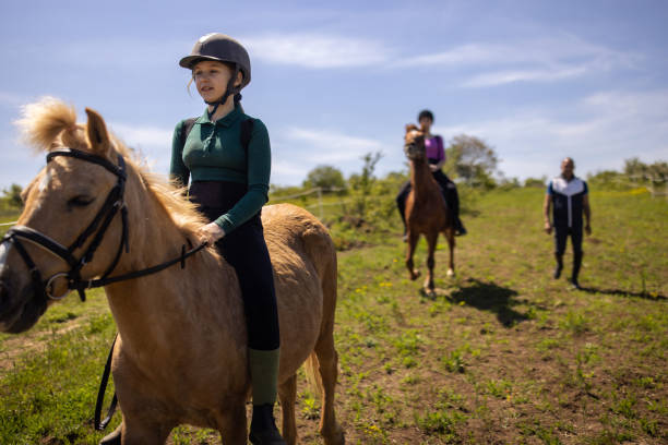 Two girls riding horses together outdoors on a meadow, their riding instructor is with them.