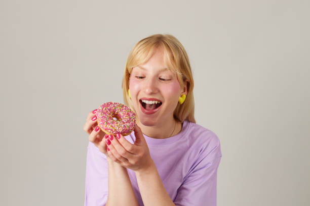 istock Young smiling woman holding a donut against grey background 1574259384