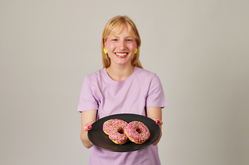 Beautiful young woman smiling, holding a plate full of delicious color donuts