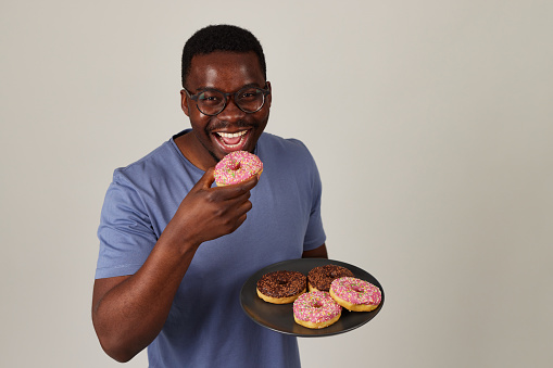 Smiling young man holding a plate full of delicious donuts against grey background