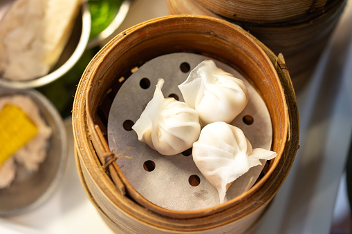 A shrimp dumpling dim sum, famous chinese appertizer food which are prepared in bamboo basket. Raw food menu object photo, close-up and selective at top.