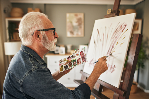 Senior man in a wheelchair painting at home