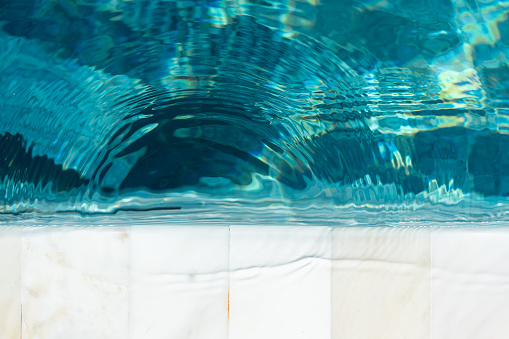 Clearly crystal turquoise blue water that reflected with sunlight at the luxury white marble swimming pool edge.