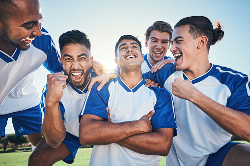 Win, football player and men celebrate together on a field for sports and fitness achievement. Happy male soccer team or athlete group with fist for challenge, competition or pride outdoor on pitch