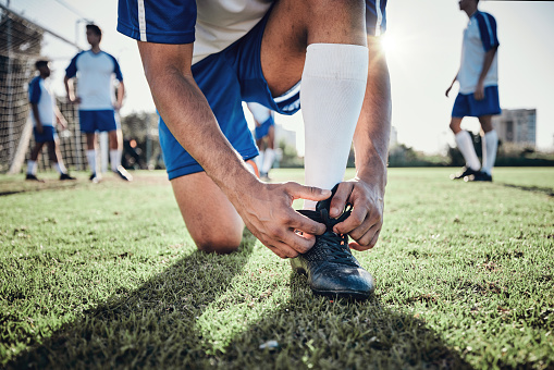 Hands, man and tie shoes on soccer field, prepare for training or fitness games. Closeup, football player or athlete getting ready with lace sneakers in sports, competition and contest on grass pitch