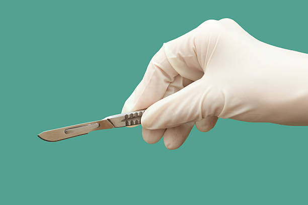 Gloved hand holding scalpel on green background  stock photo