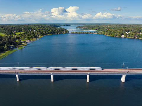 A train crossing a long bridge across a lake in a summer landscape in the Uppland region of Sweden.