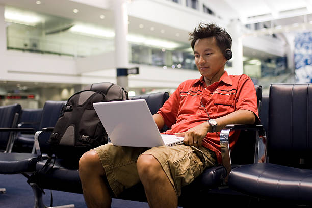 istock Asian Young Man Using Laptop and Headphones at Airport, Copyspace 157428190
