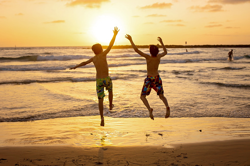 Happy teenager boys, running and playing on the beach on sunset, splashing water and jumping on the sand. Tel Aviv, Israel