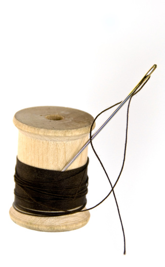 On a white background, a needle and thread with a wood spool.