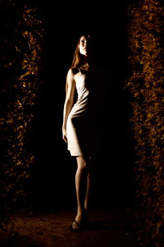 Young woman posing in the hedge maze late in the night.