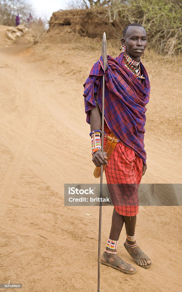 Young Maasai warrior with spear. Young masai warrior (morani) with spear and traditional pearl jewelry walking on a dusty road in Kenya, East Africa.. Adult Stock Photo