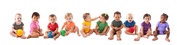 Diverse group of ten babies playing An image of babies and toddlers of various ethnicities wearing colorful onesies and sitting side by side in a long line. babies only photos stock pictures, royalty-free photos & images