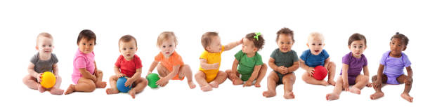 Diverse group of ten babies playing An image of babies and toddlers of various ethnicities wearing colorful onesies and sitting side by side in a long line. smiling kids on white stock pictures, royalty-free photos & images