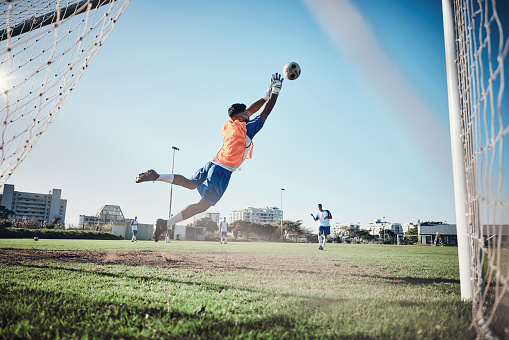 Fitness, goalkeeper or soccer player taking a penalty in a game or training match at a tournament. Save, back or male football athlete kicking ball at practice on outdoor field or pitch in stadium