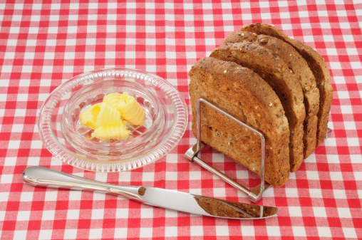 Four pieces of wholemeal or wholewheat toast in a 1930s art deco toast rack, set on a red check or gingham cloth with butter dish and knife.