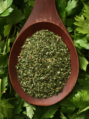 Top view of wooden spoon full of dried and ground parsley leaves