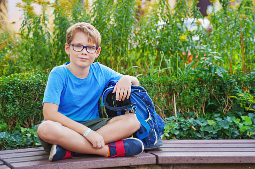 a boy with a backpack sits in the park, waiting for the bus.