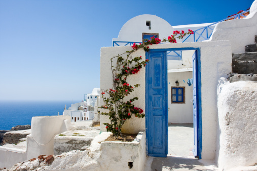 Greek Island, Cyclades. Blue wood fence entrance gate closed, red blooming bougainvillea, whitewashed wall. Traditional house exterior, Greece.