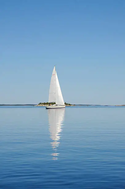 Sailboat in the archipelago of Stockholm, Sweden. White sails reflected in the water.