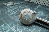 Dirty chrome shower head with limescale that should be cleaned and mold on tiles. Calcified shower due to hard water. Calcium mineral buildup.