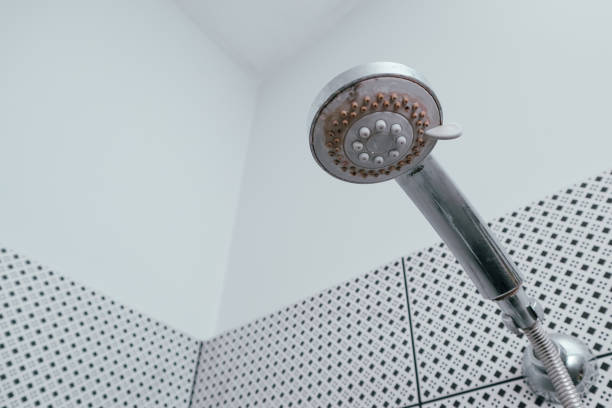 Water falling from a modern, chrome shower head against a background of white bathroom tiles.