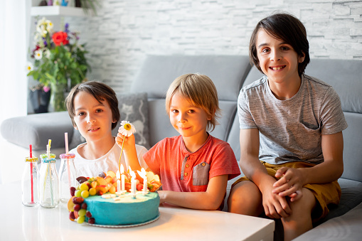 Cute preschool boy with birthday cake with candles at home, preparing for party with friends and siblings