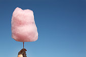Pink cotton candy being held up against a clear blue sky