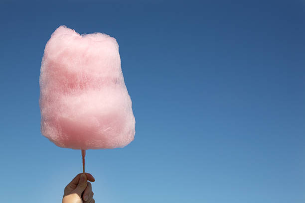 Pink cotton candy being held up against a clear blue sky Pink cotton candy in hand on blue sky with copy space candyfloss stock pictures, royalty-free photos & images