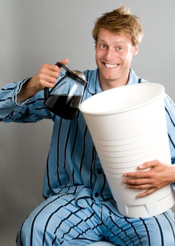 Man in pajamas pouring coffee into a gigant plastic cup. He is looking quite happy and filled with energy. 
