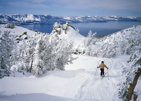 Skier above beautiful alpine lake - Lake Tahoe - in winter with a fresh snowfall covering the trees and distant mountains of the Sierra
