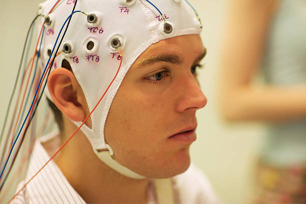 man connected with cables to computer - EEG for resarch for a scientific experiment, a young man is connected with cables to a computer, EEG for research eeg stock pictures, royalty-free photos & images