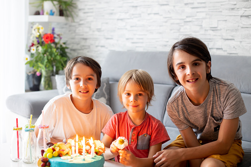 Cute preschool boy with birthday cake with candles at home, preparing for party with friends and siblings